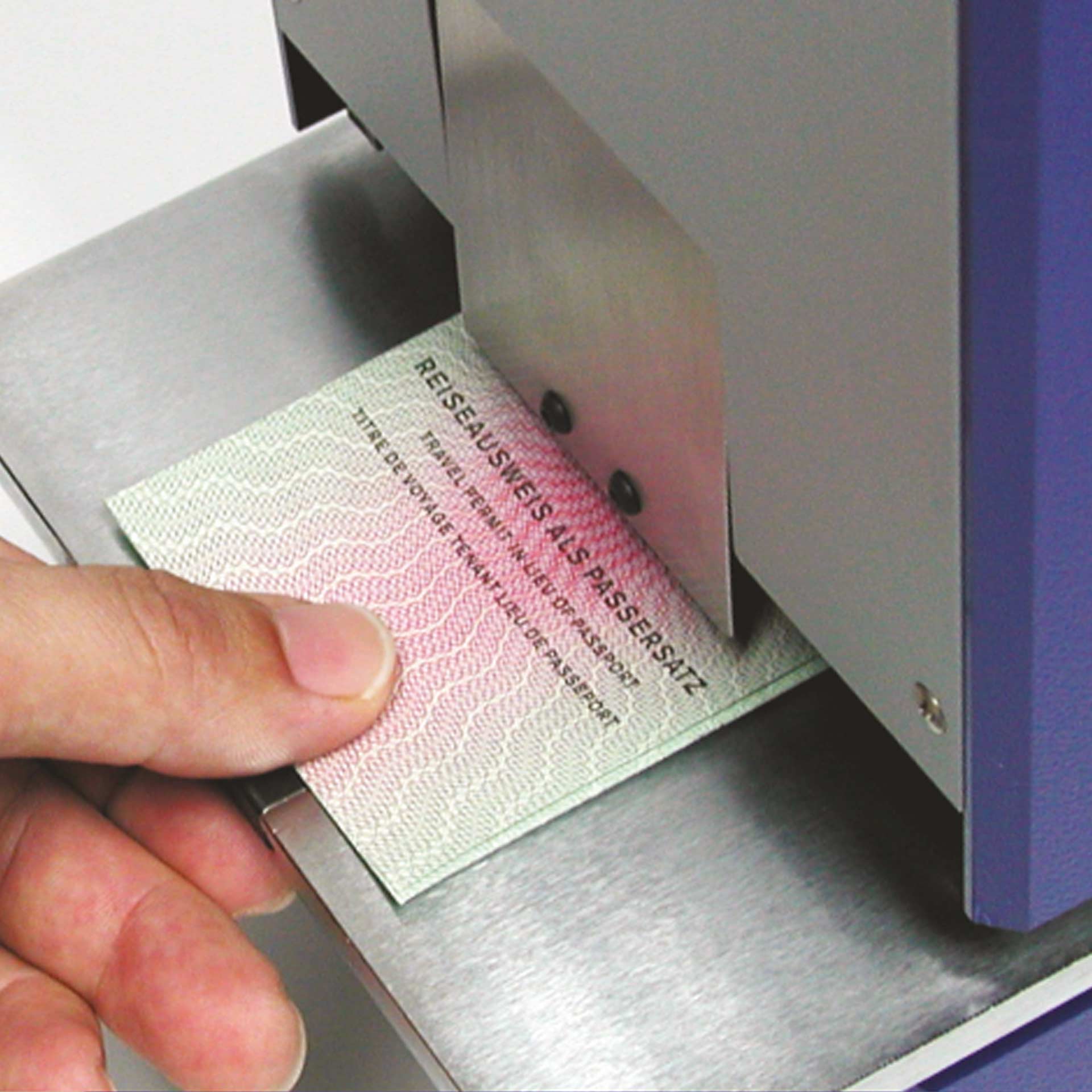 PERNUMA OFFICE L Dokument im Stanzbereich Detailansicht Detailansicht der Einfuhröffnung der PERNUMA OFFICE L Loch-Entwertungsmaschine. Eine Hand führt ein Dokument mit der Aufschrift „Reiseausweisersatz“ unter die Metallführung in den Stanzbereich.