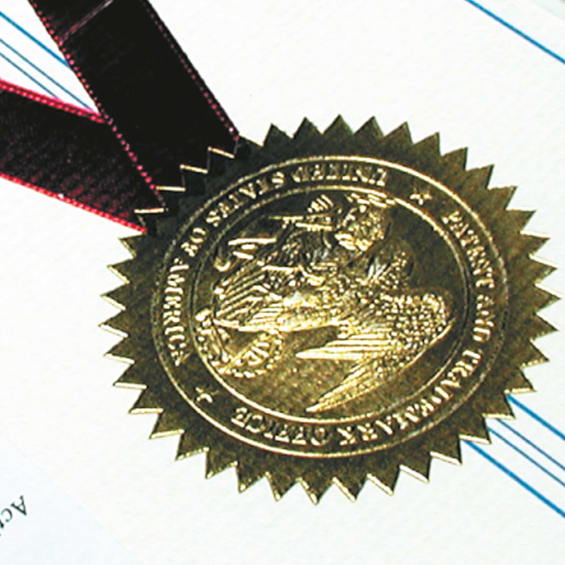 Prägesiegel auf Dokument Detailansicht Detailansicht eines goldfarbenen Prägesiegels mit gezacktem Rand auf einem Dokument, befestigt mit einem samt-weinrotem Band.