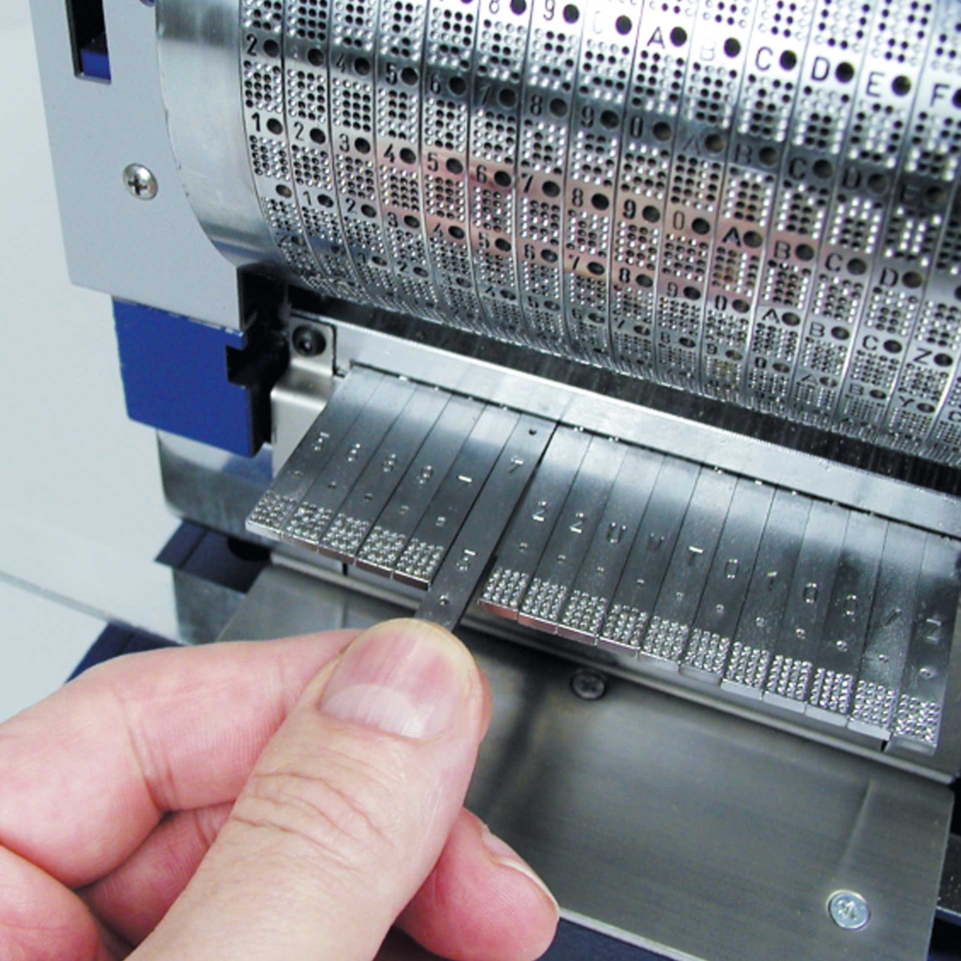 PERNUMA PERFOSTAR ES Detail Detailansicht der PERNUMA PERFOSTAR ES Perforiermaschine, Hand setzt einzelne Metallschieber mit Zeichen in die Maschine ein