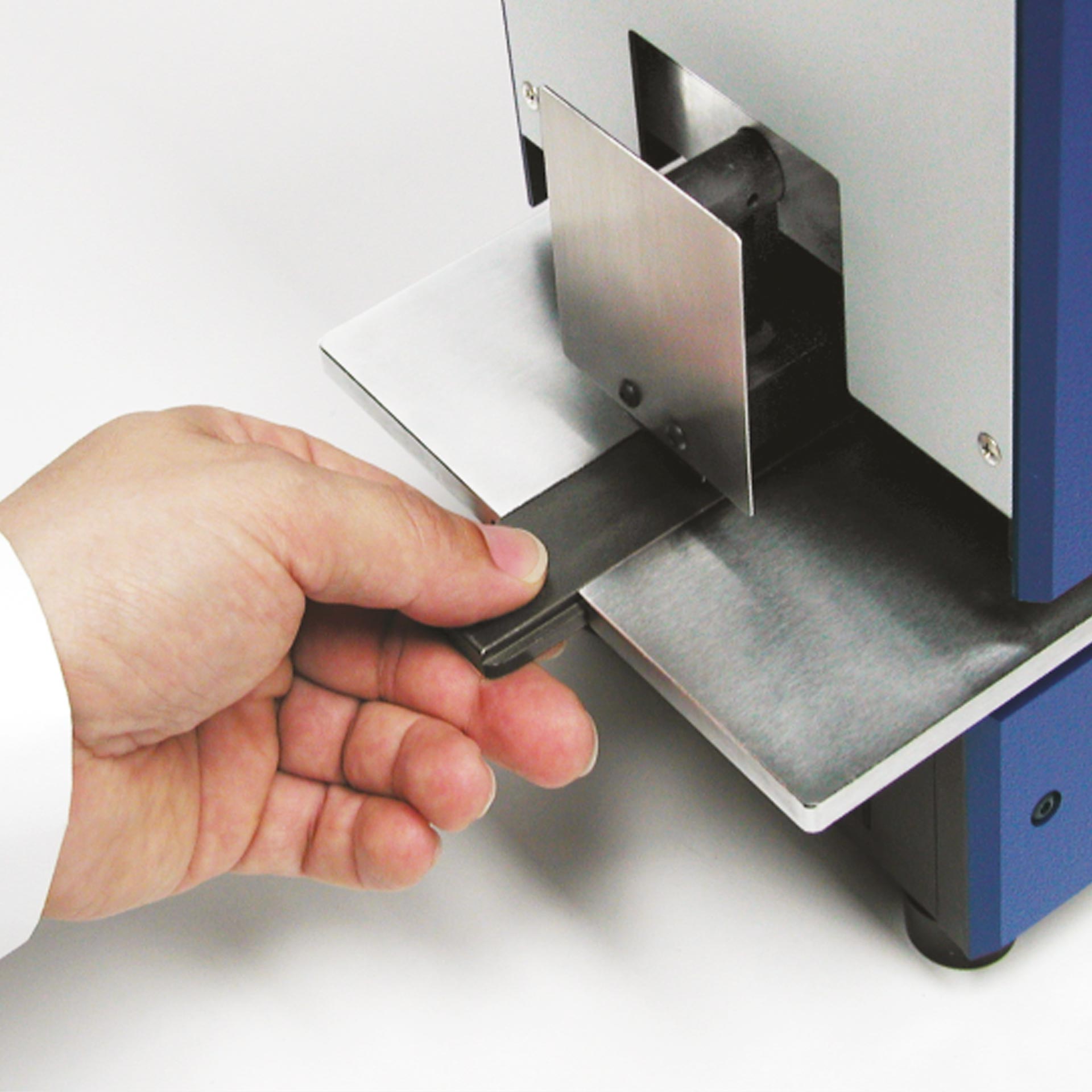 PERNUMA OFFICE L Einfuhrbereich mit Metallanschlag Detailansicht Detailansicht der Einfuhröffnung der PERNUMA OFFICE L Loch-Entwertungsmaschine. Eine Hand hält einen Metallanschlag unter der Einfuhröffnung neben der Metallauflage.