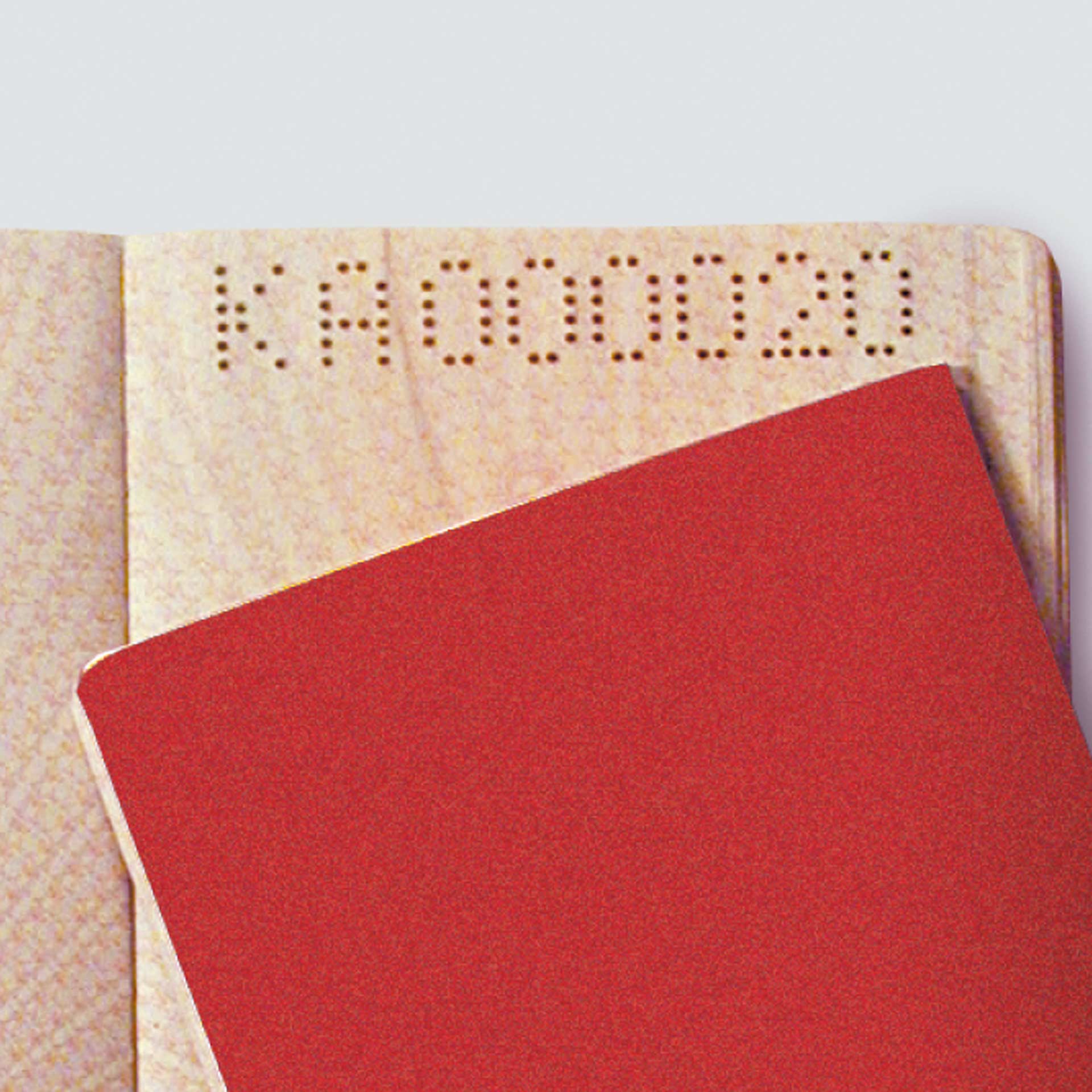 PERNUMA PERFOSTAR Beispielperforierung Detailansicht einer PERNUMA PERFOSTAR Beispielperforierung mit gelochter Buchstabenfolge auf einem Dokument, teilweise von einer roten Ausweis verdeckt.