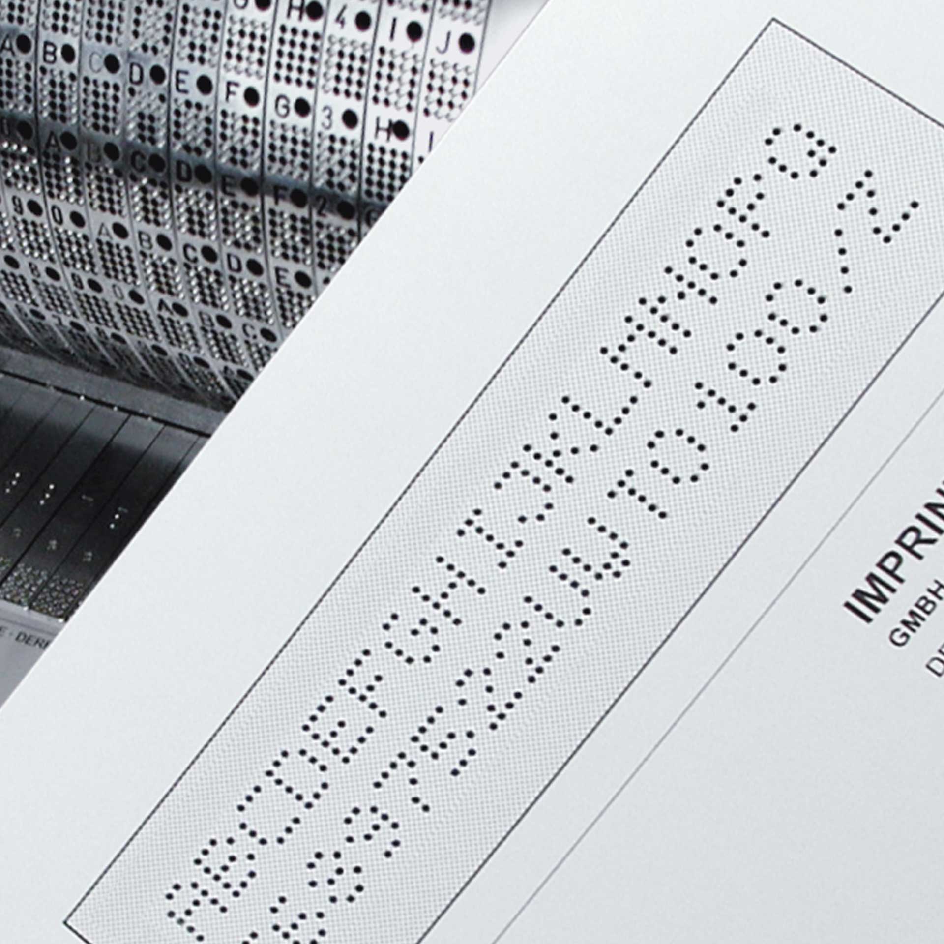 PERNUMA PERFOSTAR Beispielprägungen Detailansicht einer perforierten Beschriftung auf einem Dokument mit Buchstaben und Zahlen sowie sichtbarem Perforierwalzenbereich im Hintergrund
