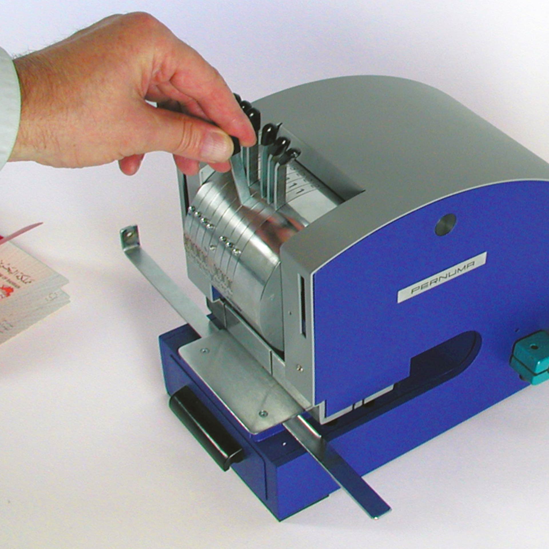 PERNUMA PERFOSTAR Perforiermaschine Anwendungsbeispiel PERNUMA PERFOSTAR Perforiermaschine bei der Einstellung des Räderwerks, Hand verstellt einzelne Einstellhebel im oberen Bereich der Maschine.