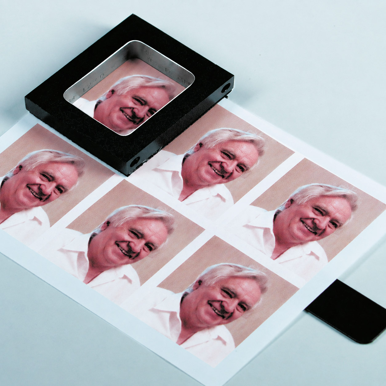 PERNUMA PERFOSET I/F beim Positionieren eines Passfotos Stanzmesser der PERNUMA PERFOSET I/F auf einem Bogen mit Passfotos, der abgerundete Ausschnitt liegt über einem Passfoto