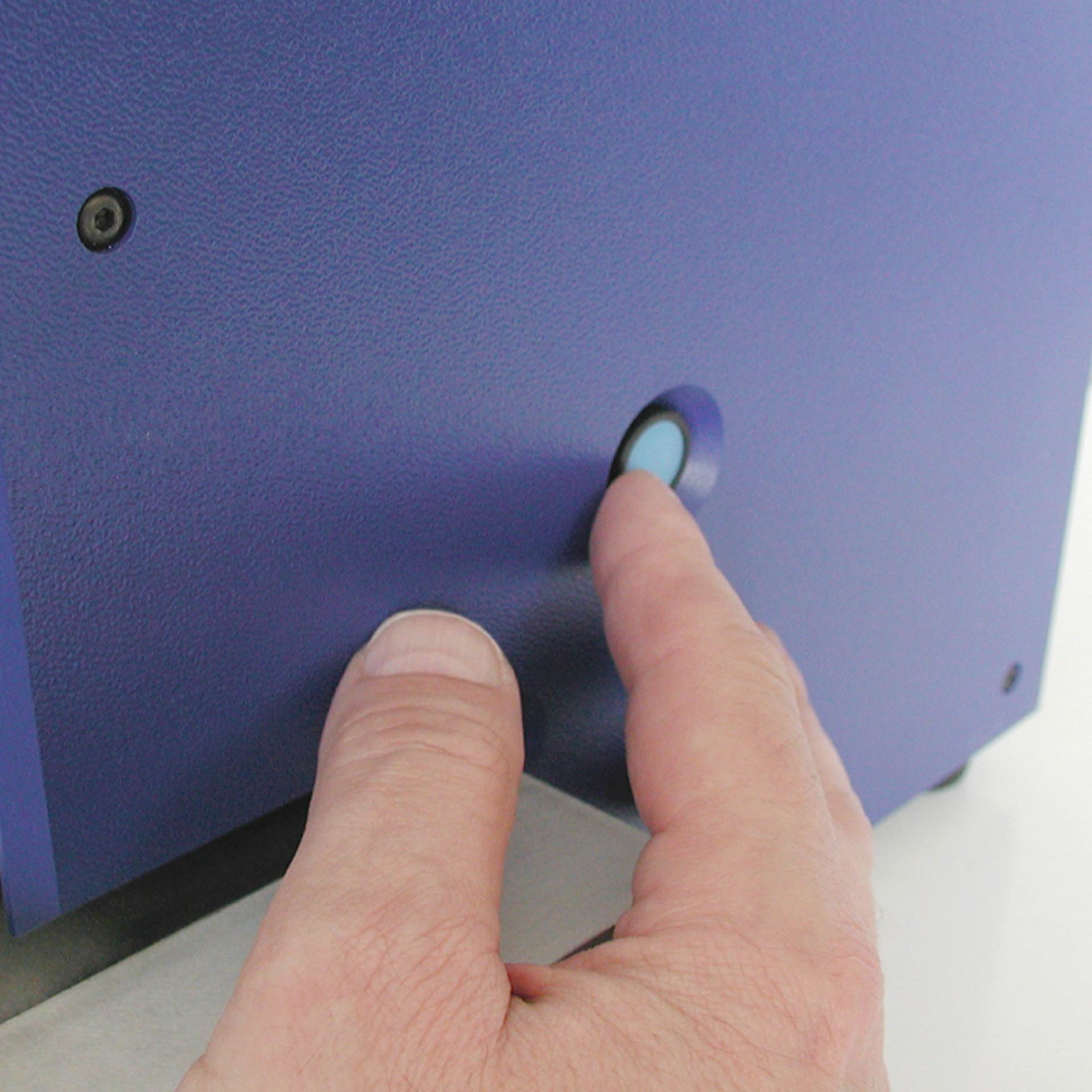 PERNUMA OFFICE T Bedienknopf Detailansicht einer Hand, die einen runden Druckknopf an der Seitenwand der Perforiermaschine betätigt