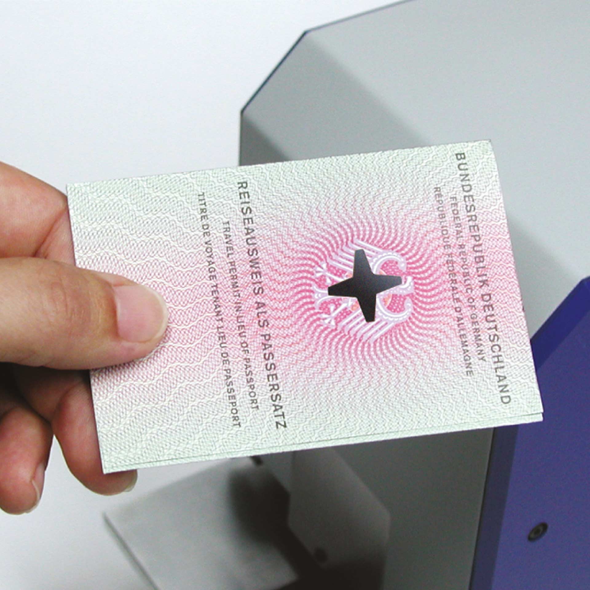 Dokument mit sternförmiger Entwertung durch PERNUMA OFFICE L Eine Hand hält ein Dokument mit der Aufschrift „Reiseausweis als Passersatz“. In der Mitte des Dokuments ist ein ausgestanztes sternförmiges Loch sichtbar, im Hintergrund ein Teil der PERNUMA OFFICE L Maschine.