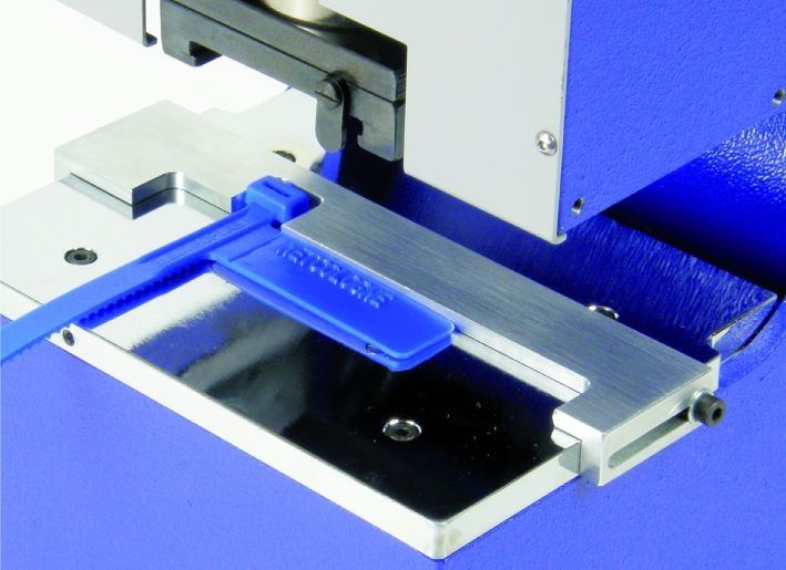 Sonderanschlag für Kabelbinder Detailansicht des Sonderanschlags an der PERNUMA METALLPRINT E mit eingelegter blauer KEKOPLAST Kabelkennzeichnungsschlaufe auf dem Anlegetisch.