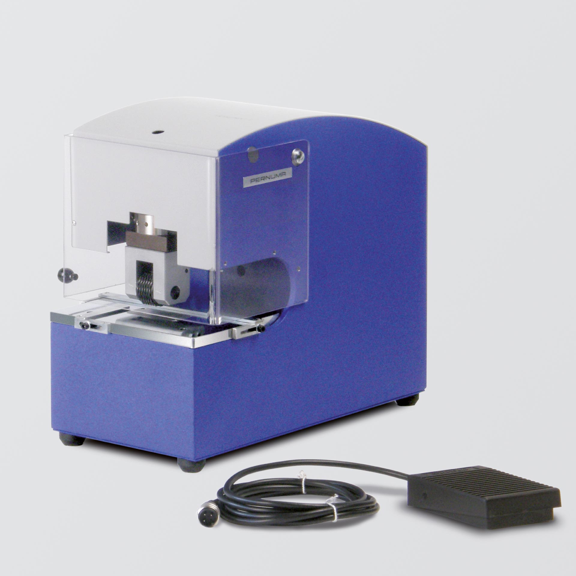 PERNUMA METALLPRINT E Prägemaschine mit Fußschalter Elektrische Prägemaschine PERNUMA METALLPRINT E in schräger Vorderansicht mit transparentem Schutzgehäuse, Prägeeinheit und angeschlossenem Fußschalter